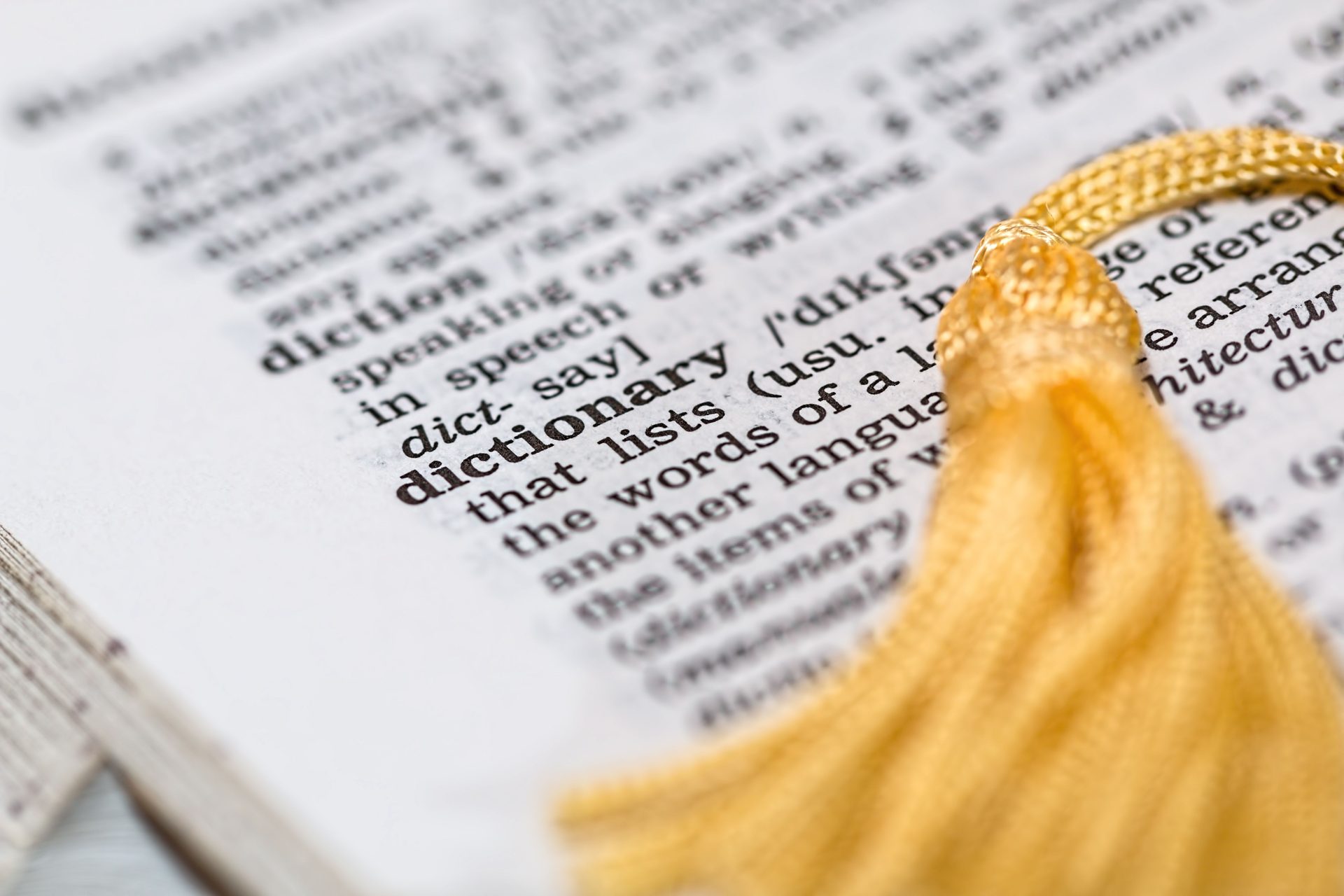 Open dictionary page with a graduation tassel resting on the word "dictionary," on UCSTAK's glossary page.