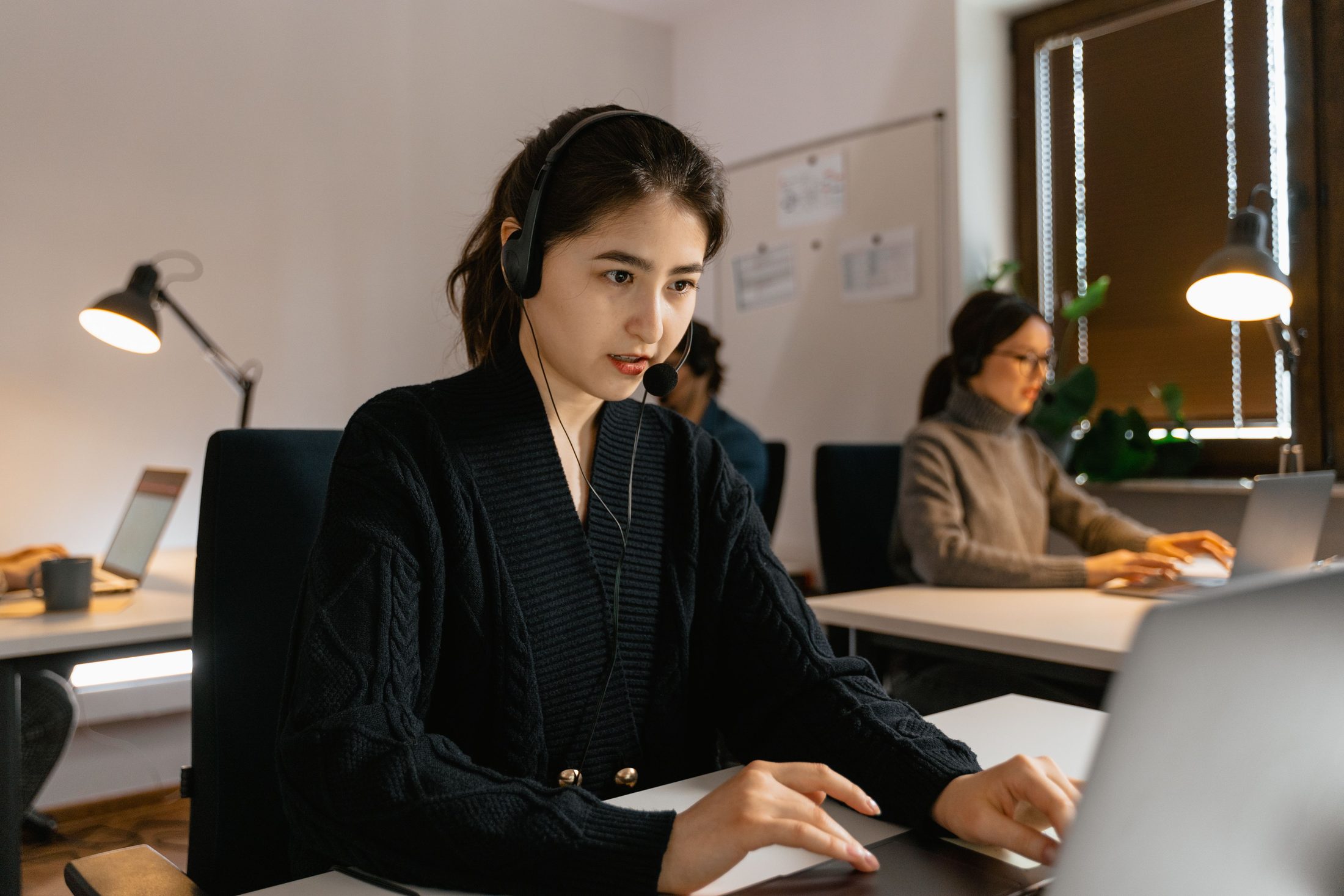 A Woman Wearing a Headset and A woman wearing a headset and using a laptop, representing UCSTAK's Chat-to-Call Escalation feature.