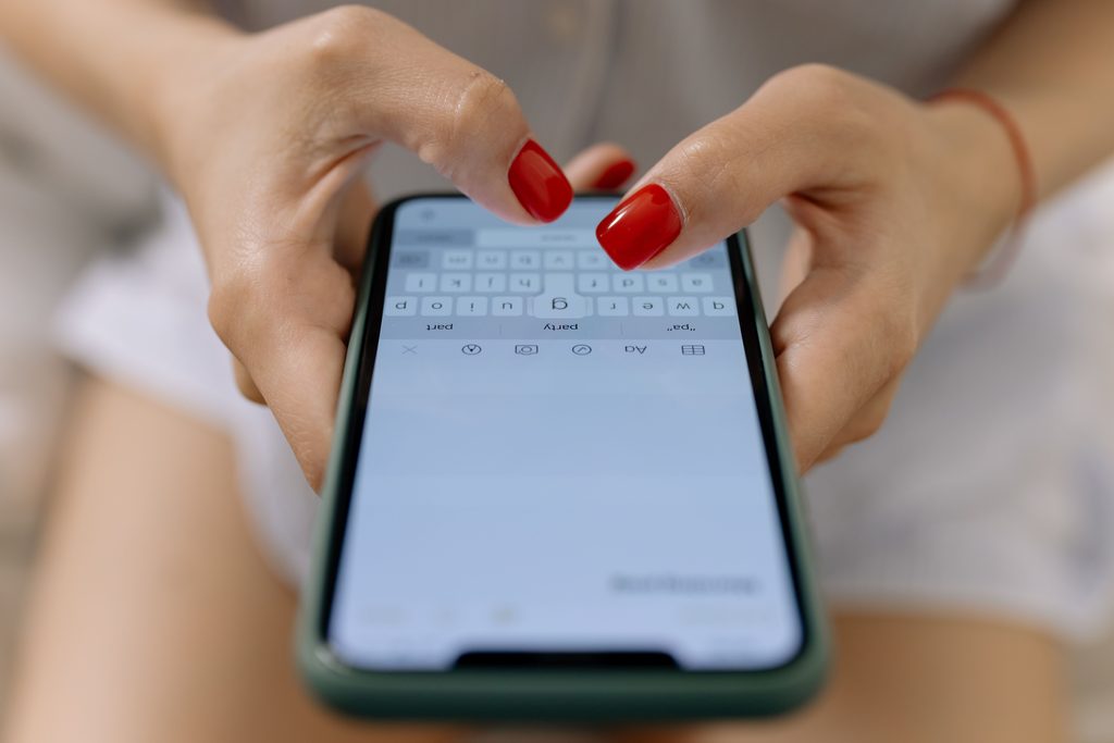 Hands of a Woman with Red Hands of a woman with red nails typing on a smartphone, representing UCSTAK's Unified Inbox Across Channels feature.