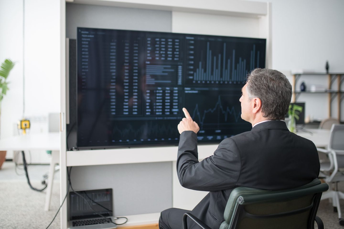 Man in black suit jacket sitting on chair while pointing his finger, representing UCSTAK's Outbound Campaign Wallboard feature.