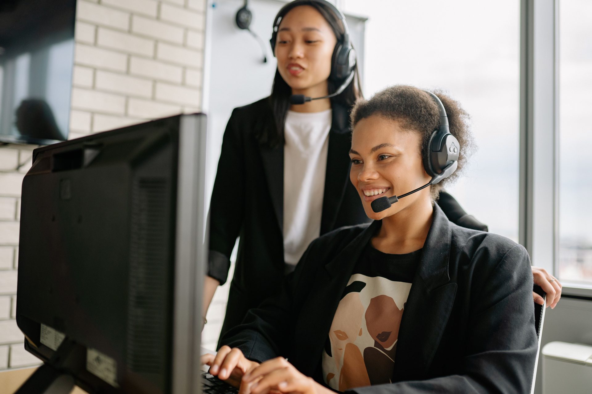 Two Women with Headsets Working As Two women with headsets working as call center agents, representing UCSTAK's Multi-Queue Agent Membership feature.