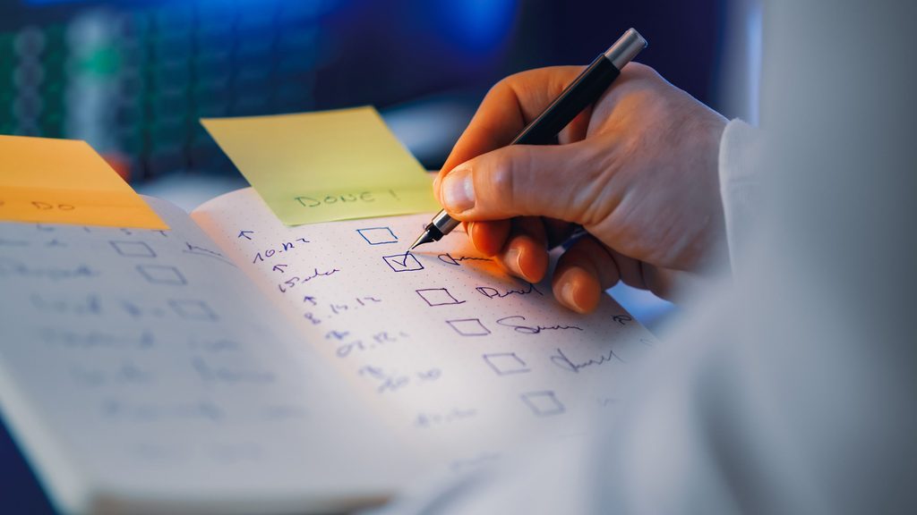 Hand Writing in Notebook with Checklist Hand writing in notebook with checklist in focus, representing UCSTAK's Priority Queues & Acceleration feature.