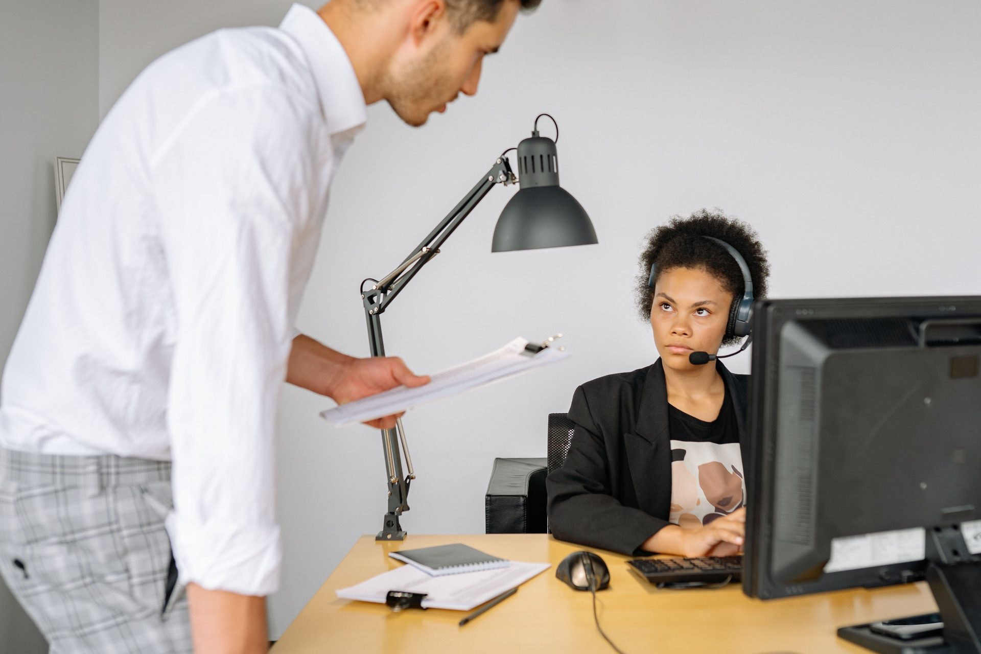 Curly Haired Woman Wearing Headset Staring Curly haired woman wearing headset staring at the man in white long sleeves, representing UCSTAK's Supervisor Tools feature.