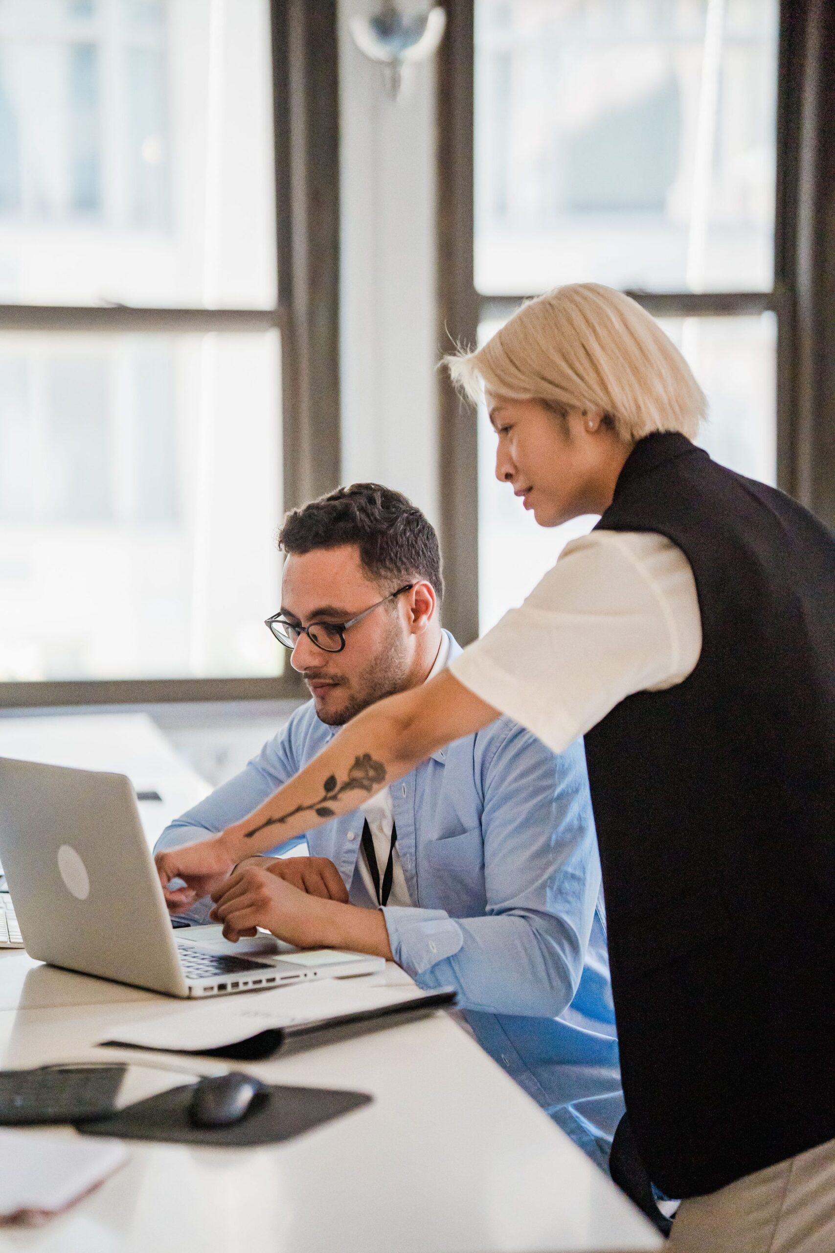 Office worker using a laptop with his colleague standing behind and pointing at the screen, representing UCSTAK's Manual Call Reassignment feature.