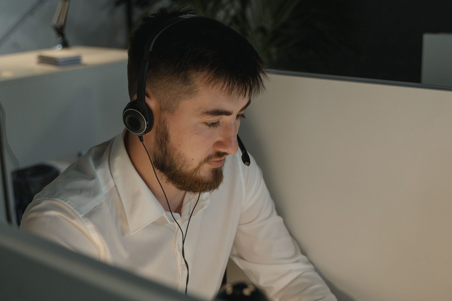 Close Up Shot of a Bearded Close up shot of a bearded man in white long sleeves wearing headphones while working in the office, representing UCSTAK's Skills-Based Routing feature.