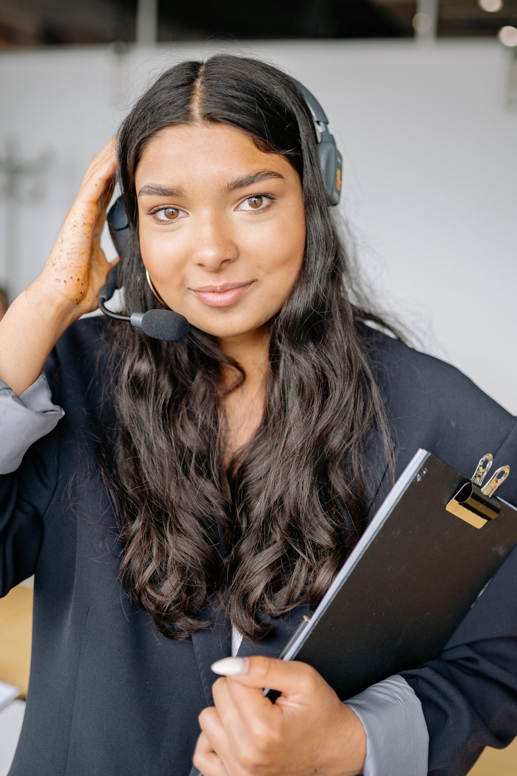 A Woman Using a Black Headphones A woman using a black headphones while holding a clipboard, representing UCSTAK's Automated AI Receptionist feature.